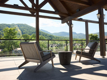 Une terrasse extérieure couverte, où se trouvent deux chaises confortables, donne sur un paysage montagneux.