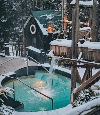 Un bain thermal entouré de neige et d’arbres à la tombée du soir.