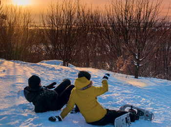 Deux raquetteurs assis sur la neige pour observer le soleil couchant