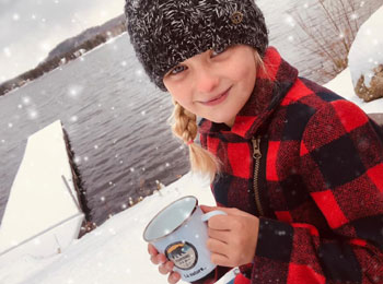 Jeune fille avec une tuque et un chandail carreauté au bord de l'eau en hiver tenant une tasse